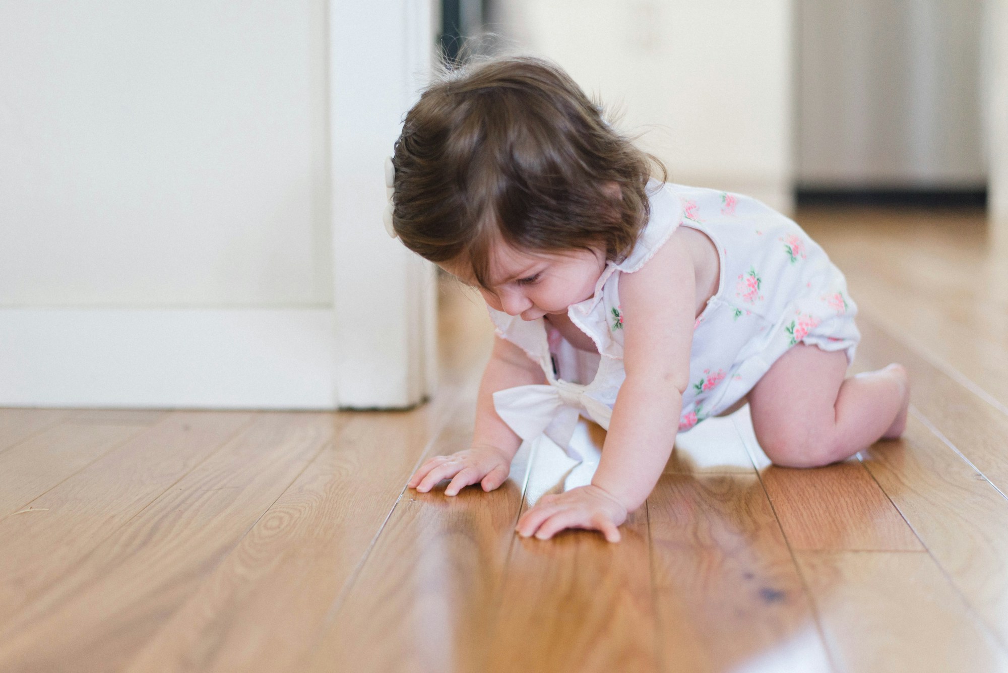 Toddler in floral dress crawling on wooden floor indoors
